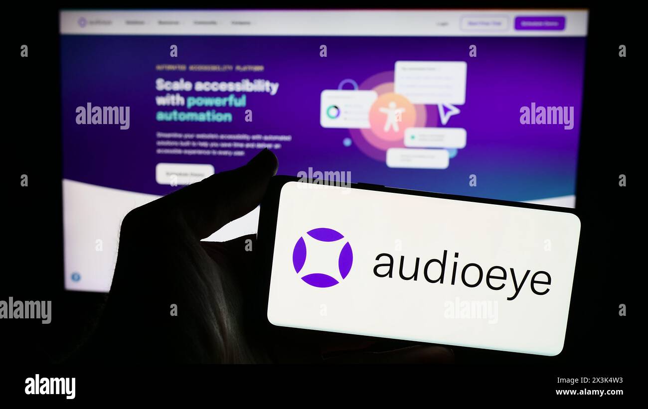 Person mit Smartphone und Logo des US-Softwareunternehmens AudioEye Inc. Vor der Website. Schwerpunkt auf dem Display des Telefons. Stockfoto