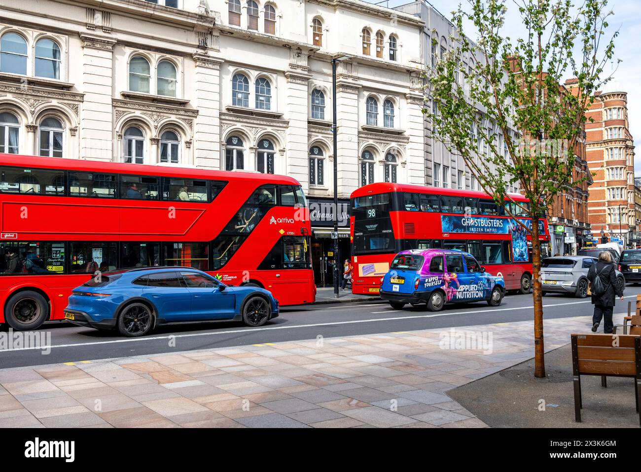 Pulsierende Straßenszene mit einem blauen Porsche Taycan und roten Londoner Bussen. Stockfoto