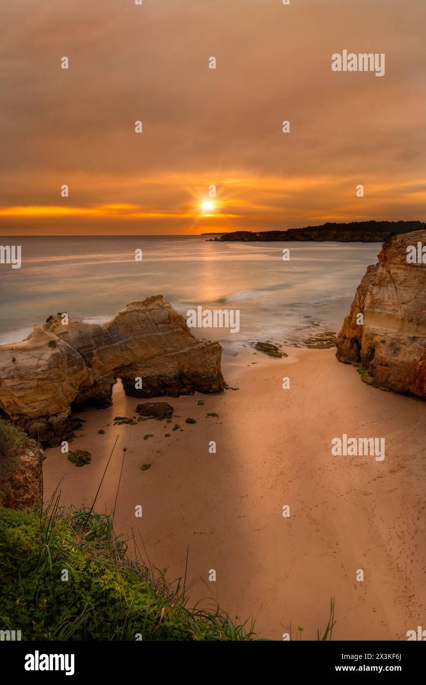 Sonnenuntergang an einem typischen Algarve-Strand in Praia da Rocha in Portugal mit den Wellen am Strand und dem Sonnenlicht, das durch eine Höhle scheint Stockfoto