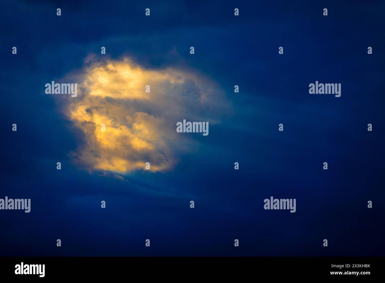 Beeindruckendes Bild, das eine einzelne Wolke erfasst, die hell durch Sonnenlicht vor einem dunklen Dämmerhimmel beleuchtet wird. Diese Szene weckt Gefühle der Hoffnung und Isolation. Stockfoto