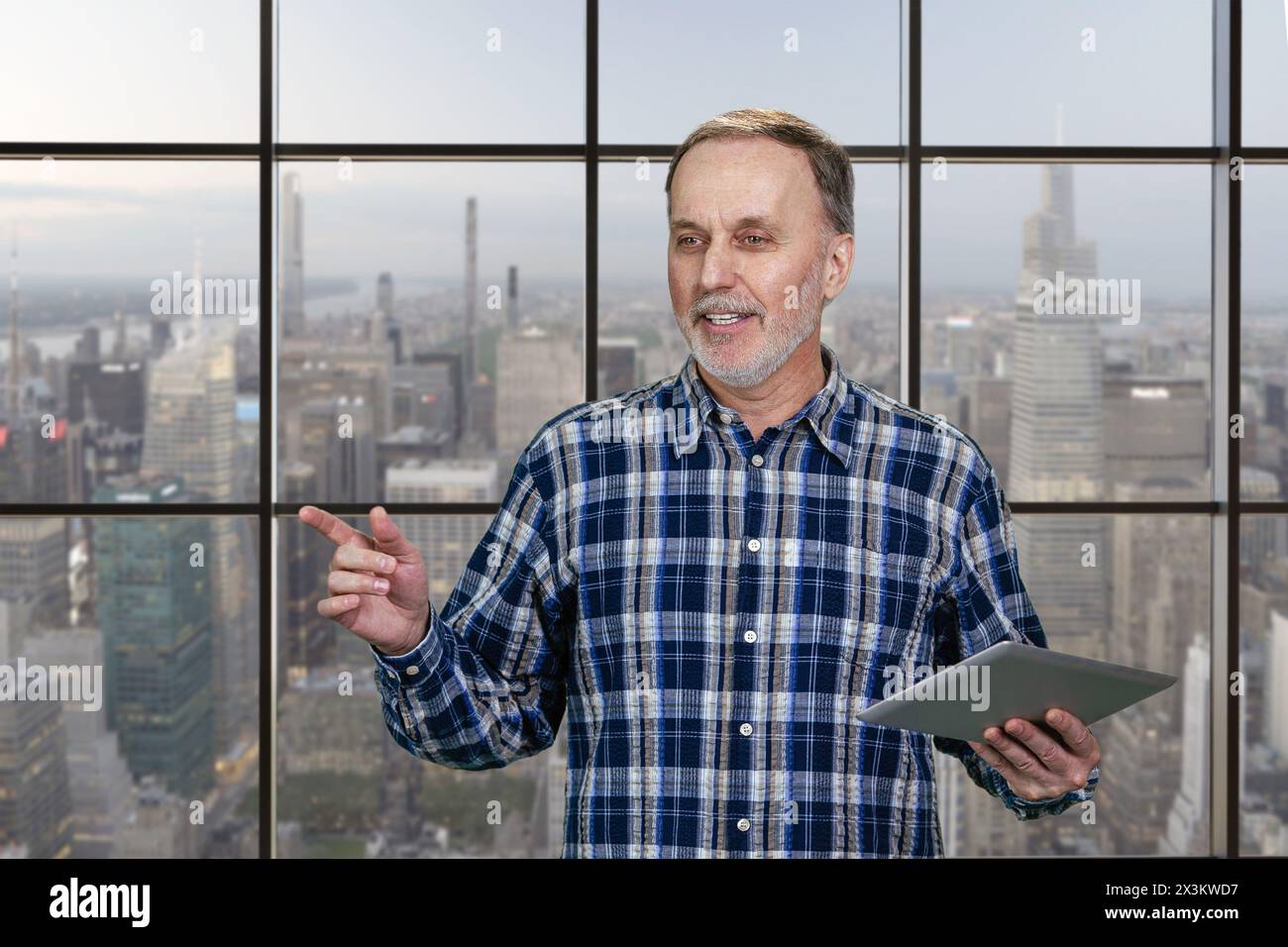 Glücklicher, fröhlicher alter Mann mit Tablet-pc. Karierte Fenster im Hintergrund mit Blick auf die Stadt. Stockfoto