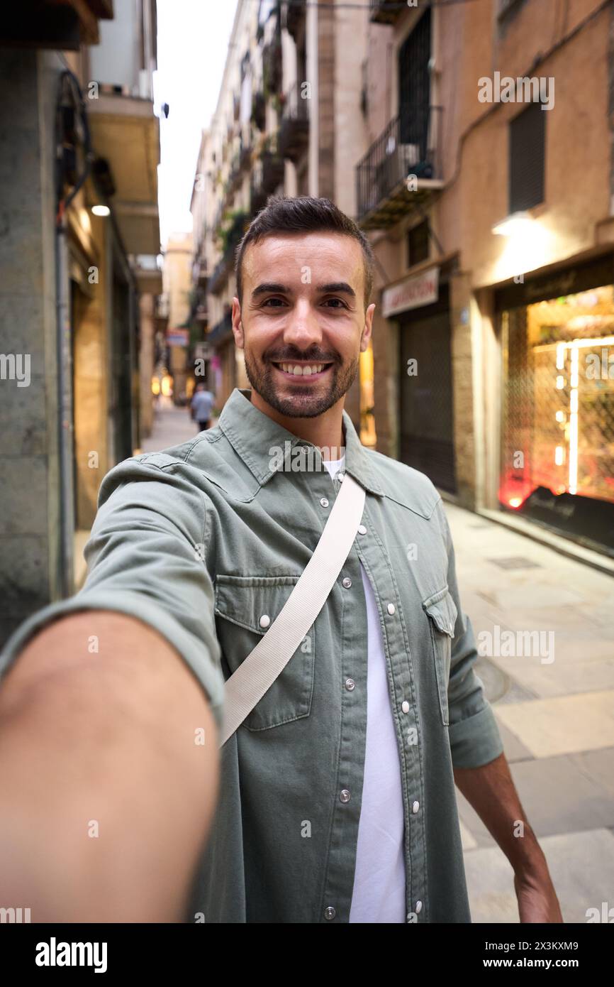 Junger Erwachsener glücklicher kaukasischer Mann, der ein lächelndes Selfie auf der touristischen Straße Madrids im Hintergrund macht. Stockfoto