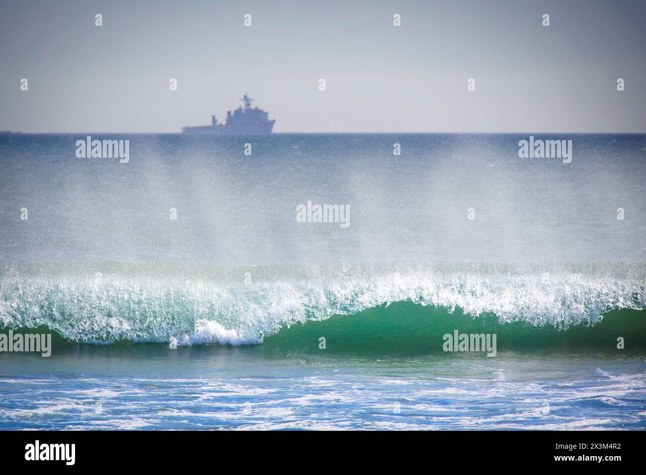 Der Pazifik-Ozean-Surf rollt ein, während ein Navy-Schiff am fernen Horizont in Coronado, Kalifornien, sitzt. Stockfoto