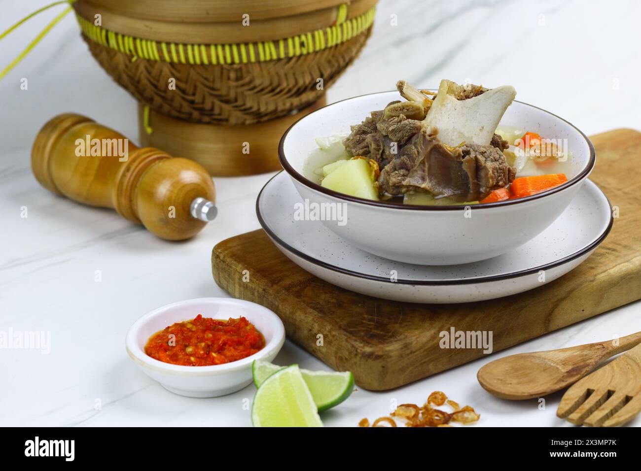 Sopp Daging sapi oder indonesische Rindfleischsuppe, serviert auf einer weißen Keramikschale mit Sambal und Limettenscheiben. Selektiver Fokus mit weißem Marmorhintergrund. Stockfoto