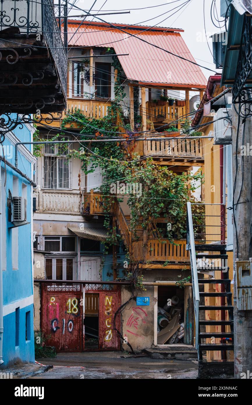 Ein bezaubernder, verwitterter Innenhof in Tiflis Altstadt mit farbenfrohen Balkonen, kriechendem Efeu und rustikalen Holztreppen, die sich in der Decke verheddert haben Stockfoto