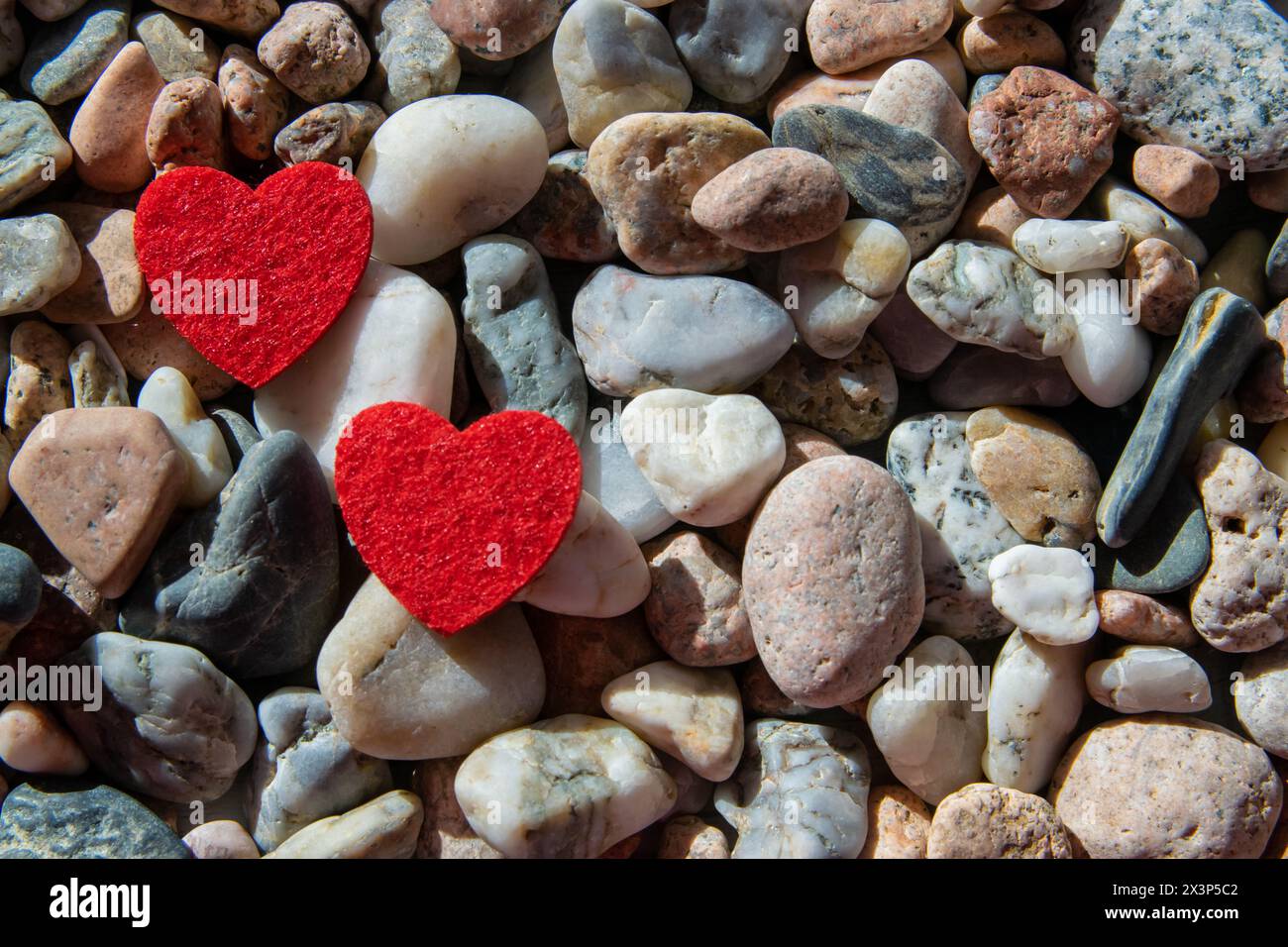 Zwei rote, helle Stoffherzen auf anderen Steinen in der Nähe des Flusses. Romantischer Hintergrund. Stockfoto