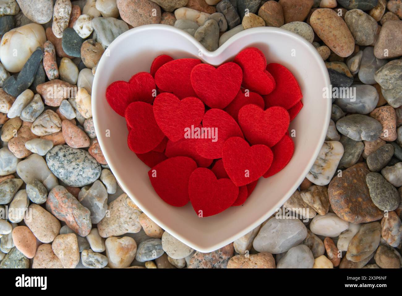 Schöne rote helle Stoffherzen in romantischer Herzform auf Flusssteinen. Stockfoto