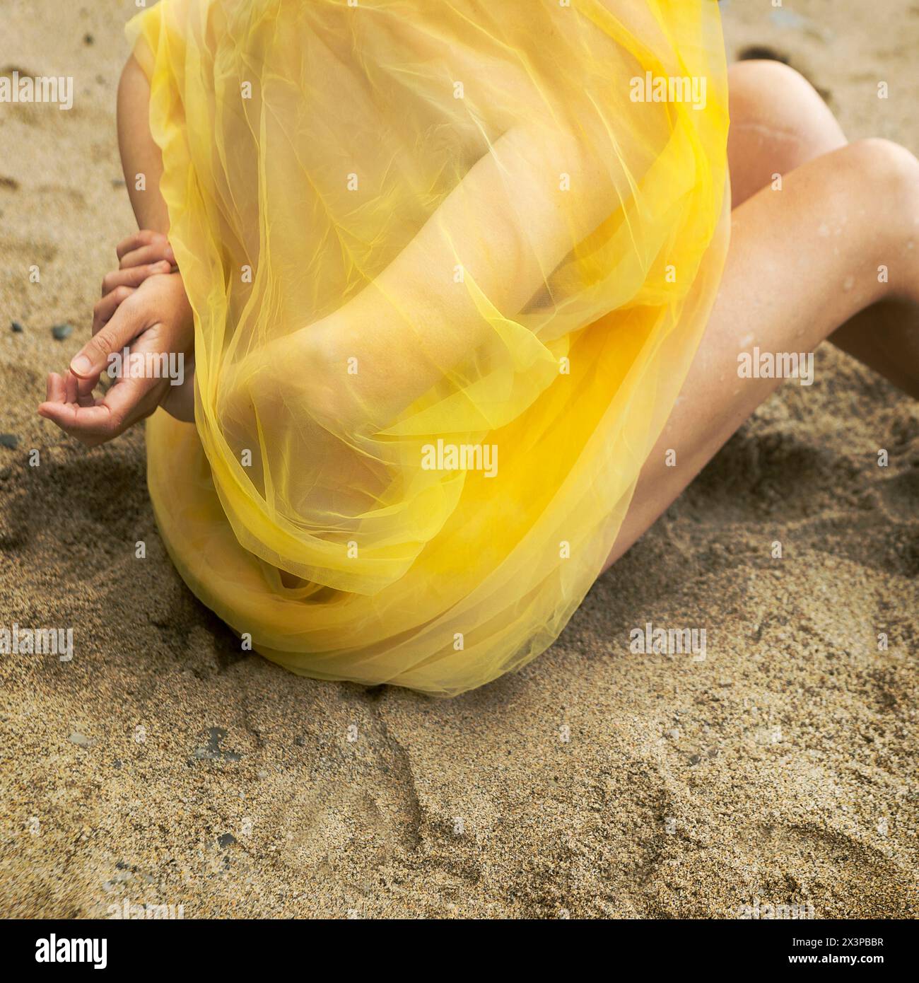 Frau mit gelbem Tüll bedeckt, sitzt auf dem Sand eines asturischen Strandes III, Spanien Stockfoto