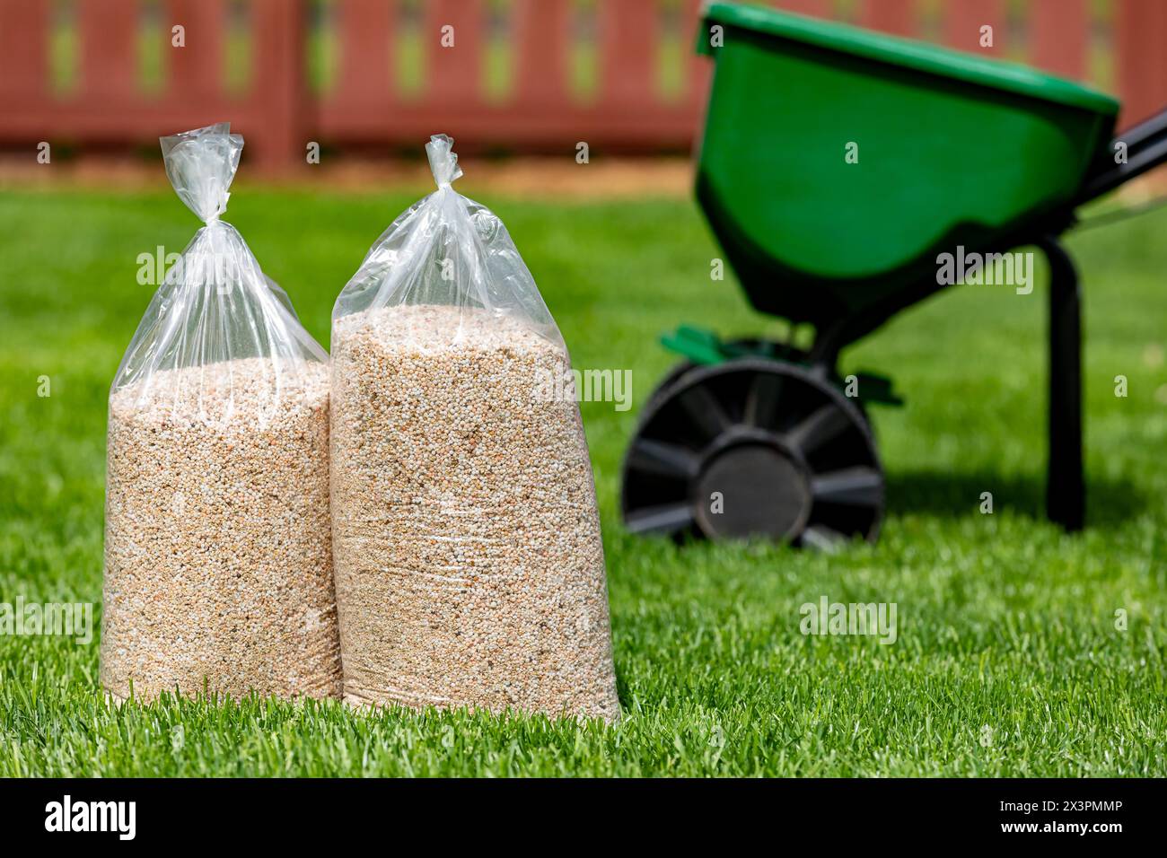 Säcke mit Rasendünger und Herbizid mit Rundstreuer auf dem Hof mit gesundem Gras. Rasenpflege, Unkrautbekämpfung und Landschaftsgestaltung. Stockfoto