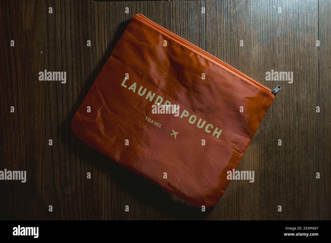 Orangefarbene Wäschetasche auf dem Holzboden für Reisen mit flachem Lagewinkel Stockfoto