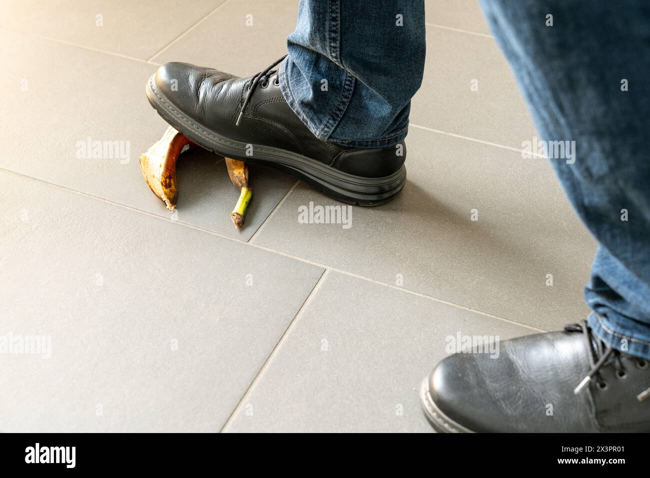 Nahaufnahme eines Mannes in schwarzen Schuhen, der beim Gehen auf eine Bananenschale tritt. Begriff der Stolpergefahr oder Sturzgefahr. Nur die Füße sichtbar. Stockfoto