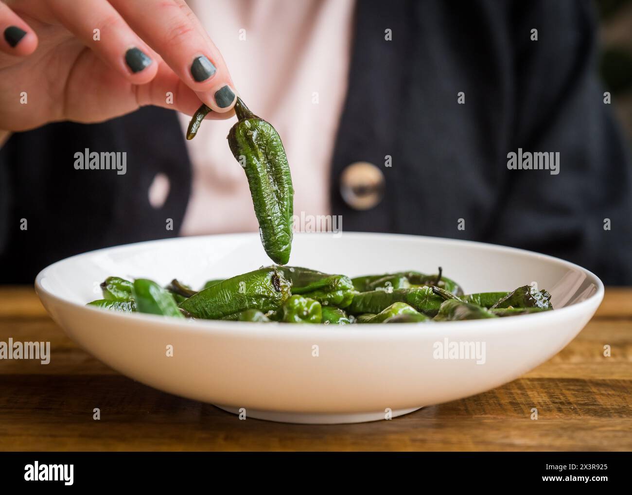 Gebackener grüner Mini-Pfeffer mit Salz wird von einem Teller in einem Café-Restaurant abgeholt Stockfoto