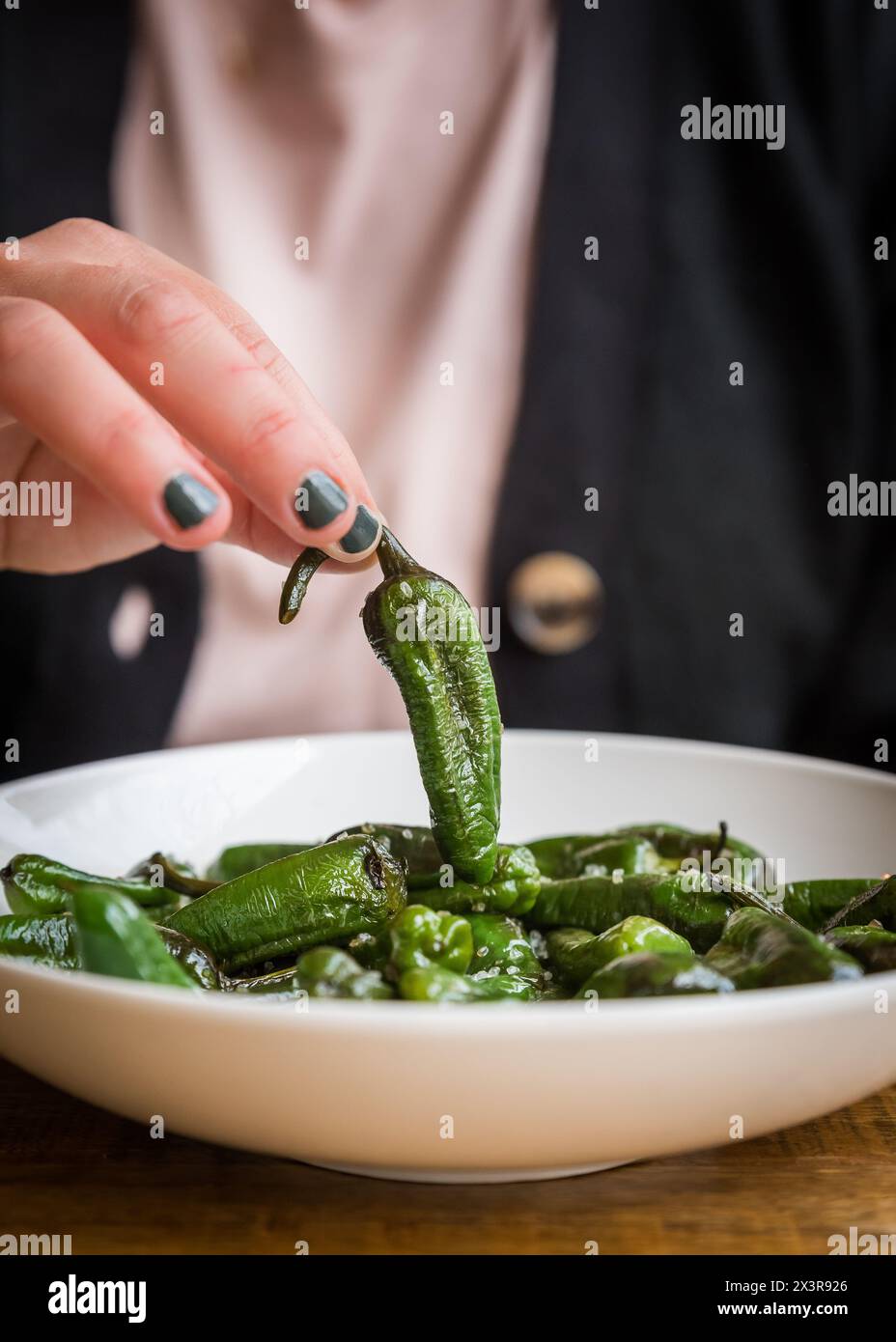 Gebackener grüner Mini-Pfeffer mit Salz wird von einem Teller in einem Café-Restaurant abgeholt Stockfoto