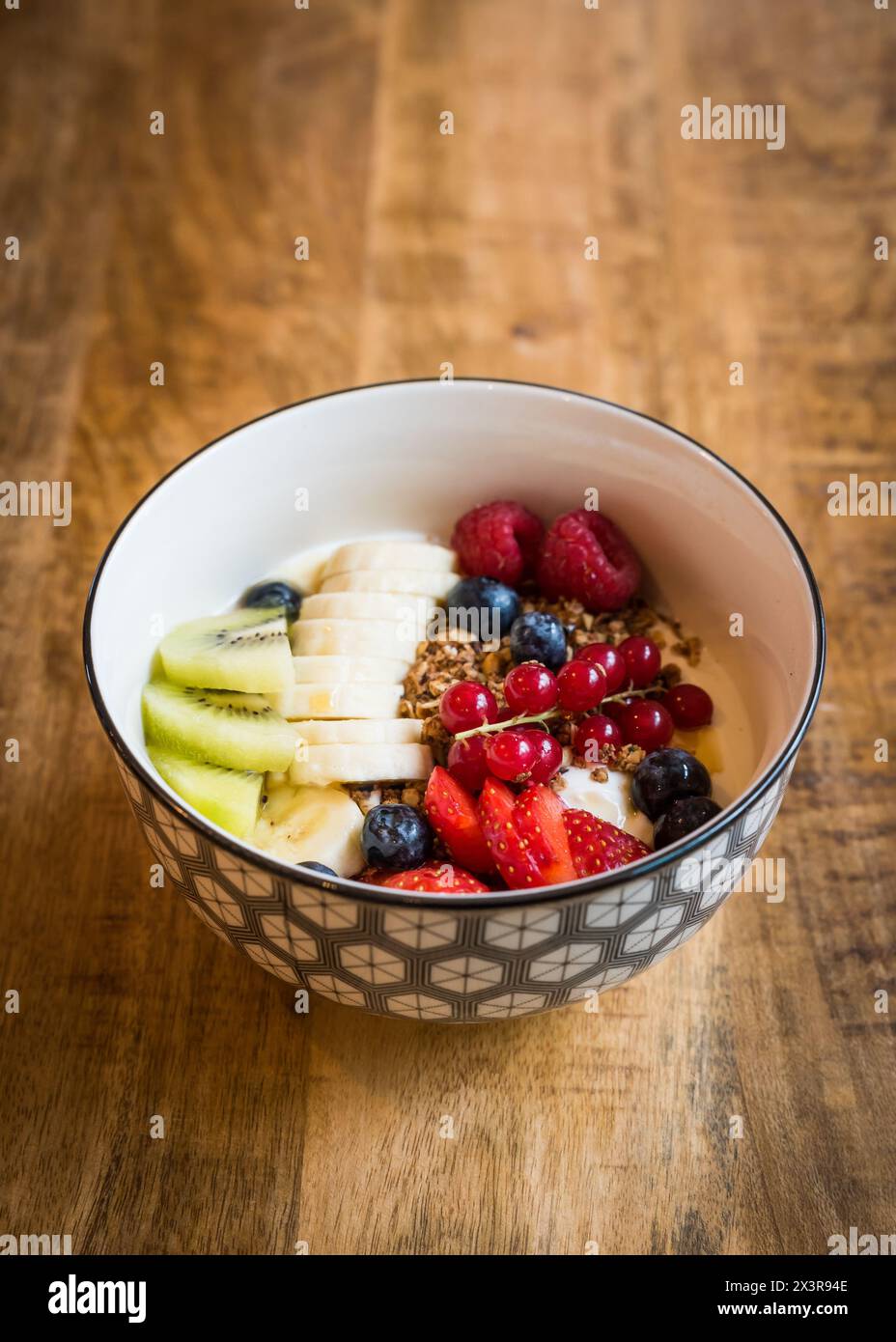 Schüssel mit frischem Joghurt mit Müsli, gemischten Sommerbeeren, Banane und Kiwi auf einem Holztisch Stockfoto