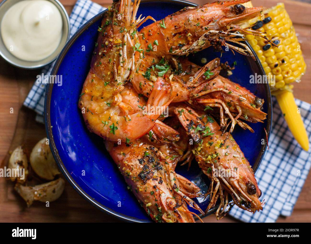 Nahansicht von oben auf gebratene Garnelen mit Knoblauch in blauer Schüssel mit Mais und Mayonnaise auf Holztisch Stockfoto