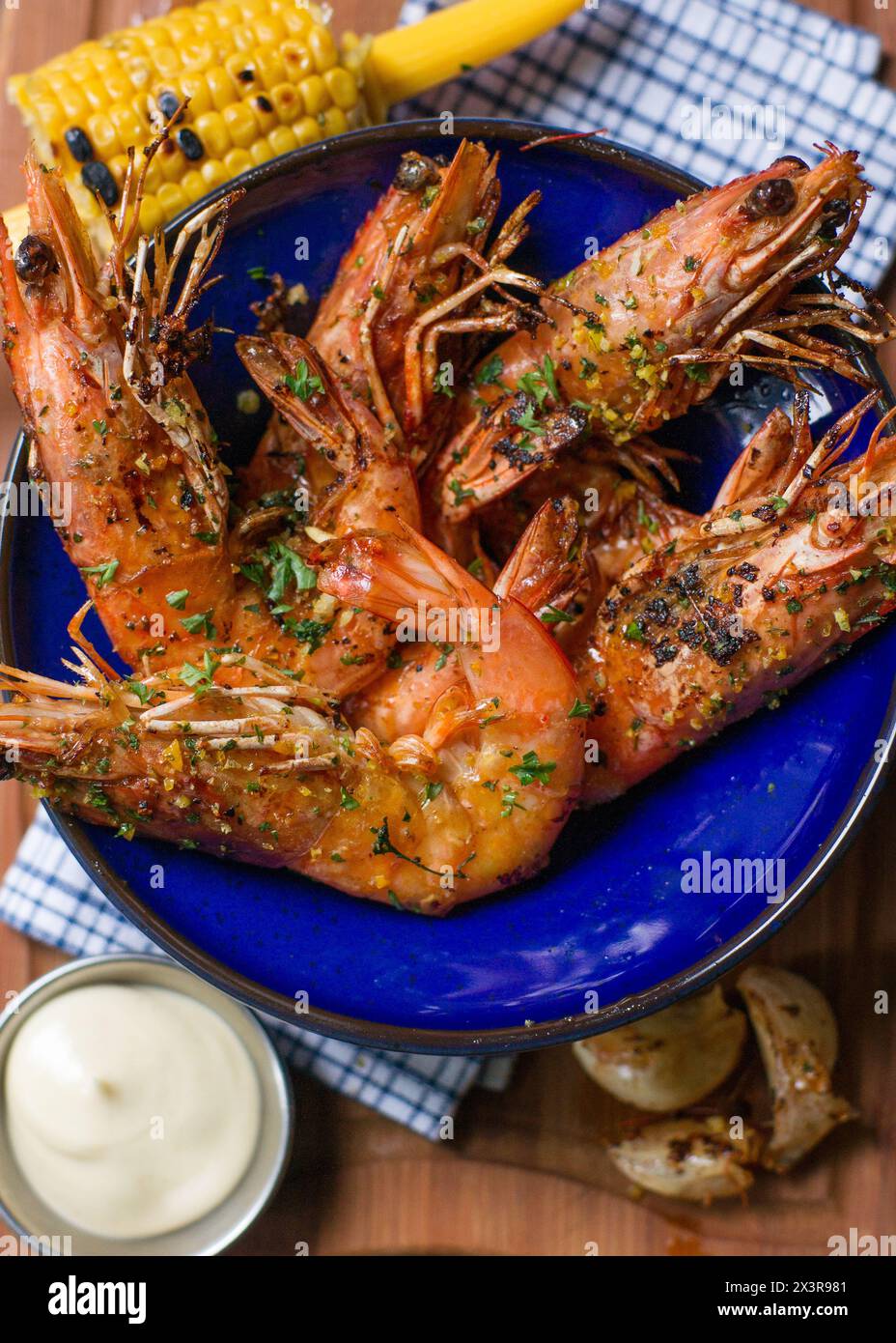 Nahansicht von oben auf gebratene Garnelen mit Knoblauch in blauer Schüssel mit Mais und Mayonnaise auf Holztisch Stockfoto