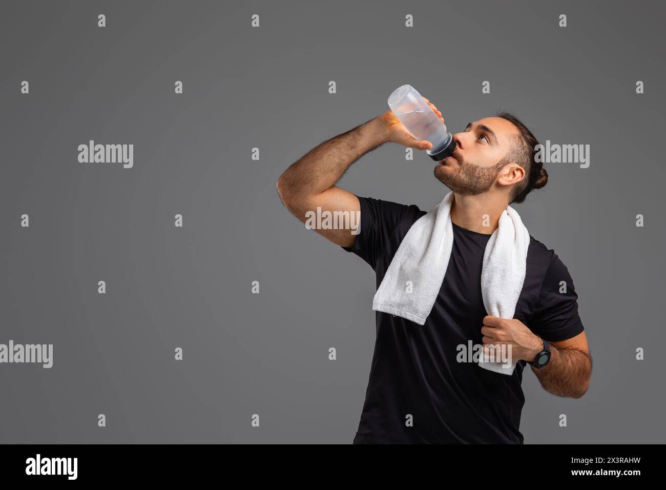 Ein Mann trinkt Wasser aus einer Flasche auf grauem Hintergrund Stockfoto