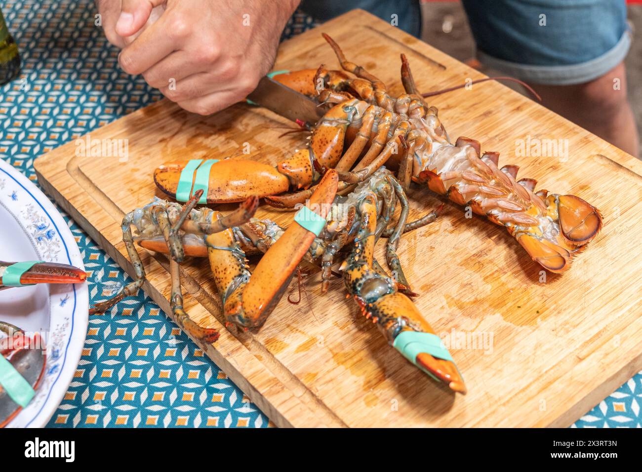 Die Hand des Mannes schneidet Hummerschwänze mit einem Messer auf einem Holzbrett Stockfoto