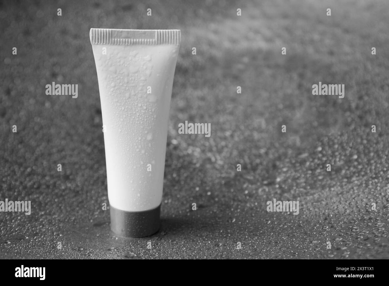 Feuchtigkeitsspendende Creme in der Tube auf dunklem feuchtem Hintergrund, Nahaufnahme. Leerzeichen für Text Stockfoto