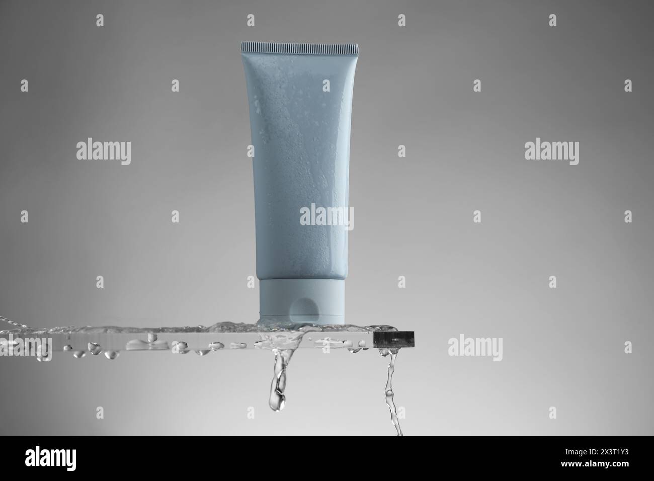 Feuchtigkeitsspendende Creme in der Tube auf Glas mit Wassertropfen vor grauem Hintergrund Stockfoto
