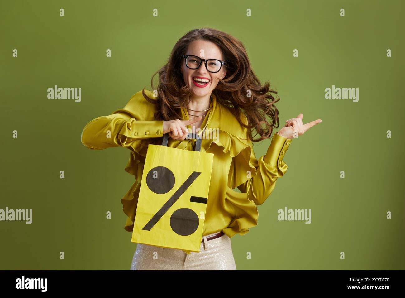 Lächelnde Frau isoliert auf grünem Hintergrund in grüner Bluse und Brille mit Verkauf Einkaufstasche. Stockfoto