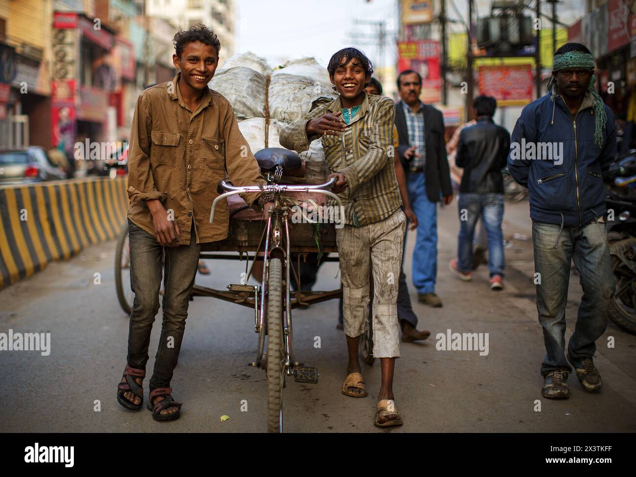 Zwei junge Männer, die einen Fahrradträger auf einer Straße in Varanasi, Indien, schieben. Stockfoto