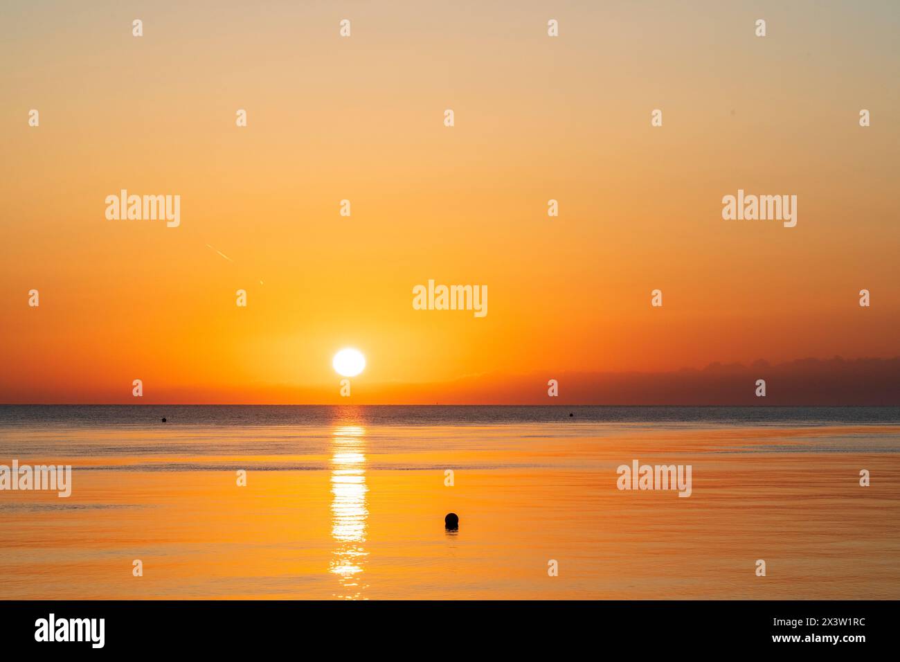 Sonnenaufgang über einem sehr ruhigen Meer in Herne Bay an der Küste von Kent. Dünne Wolkenschicht am Horizont, über der die Sonne scheint, das Meer hat eine orange Farbe. Stockfoto