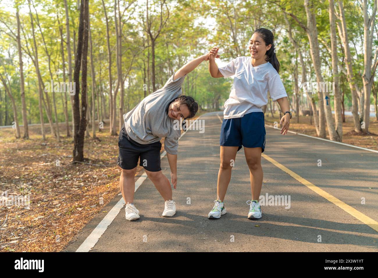 Zwei junge Freundinnen, die ihre Arme und Beine Strecken, bevor sie ihren morgendlichen Lauf in einem lokalen Laufpark beginnen Stockfoto