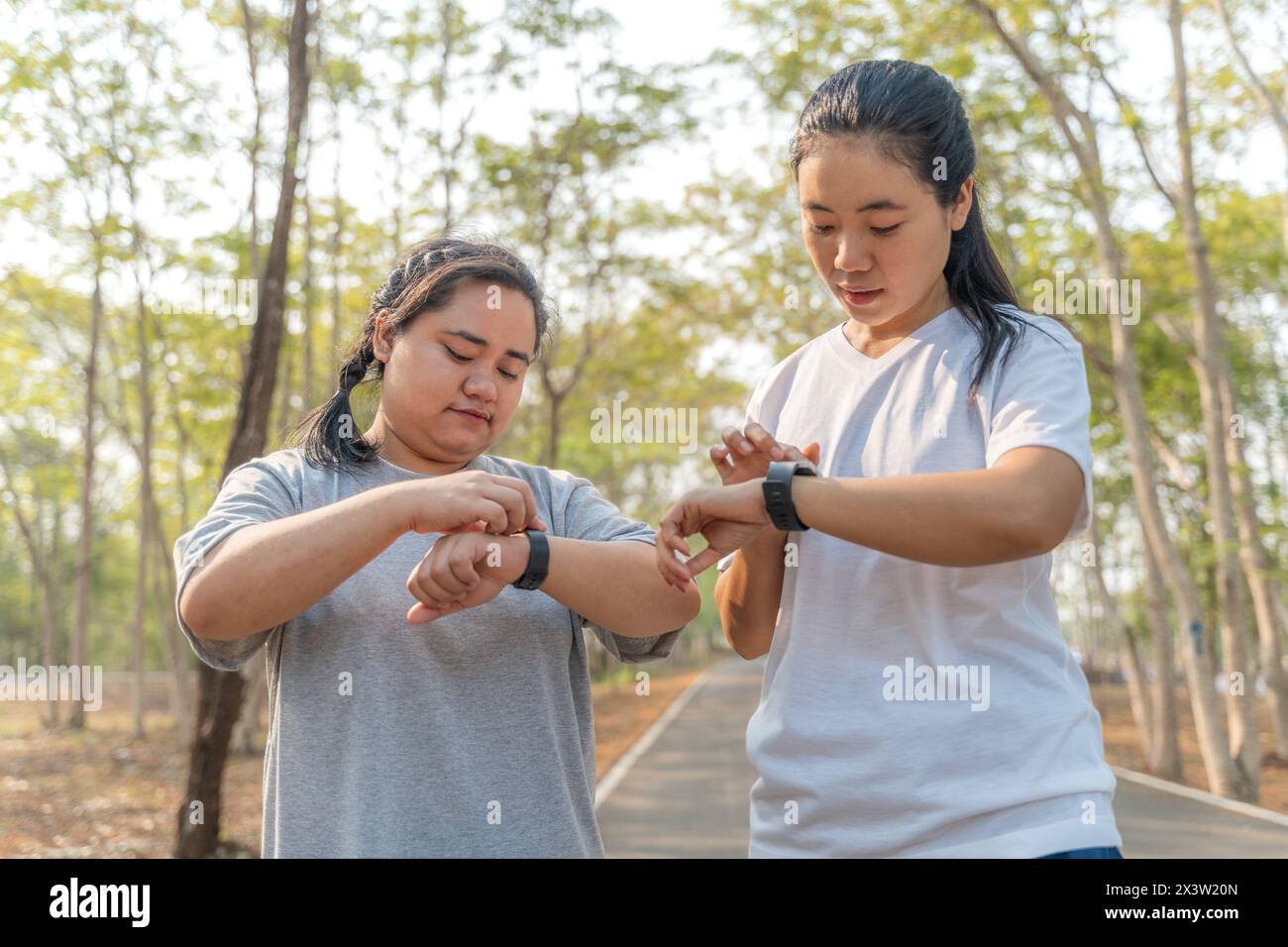 Zwei junge Freundinnen, die ihre Laufzeit auf ihrer Smart Watch nach ihrem morgendlichen Lauf in einem lokalen Laufpark überprüfen Stockfoto