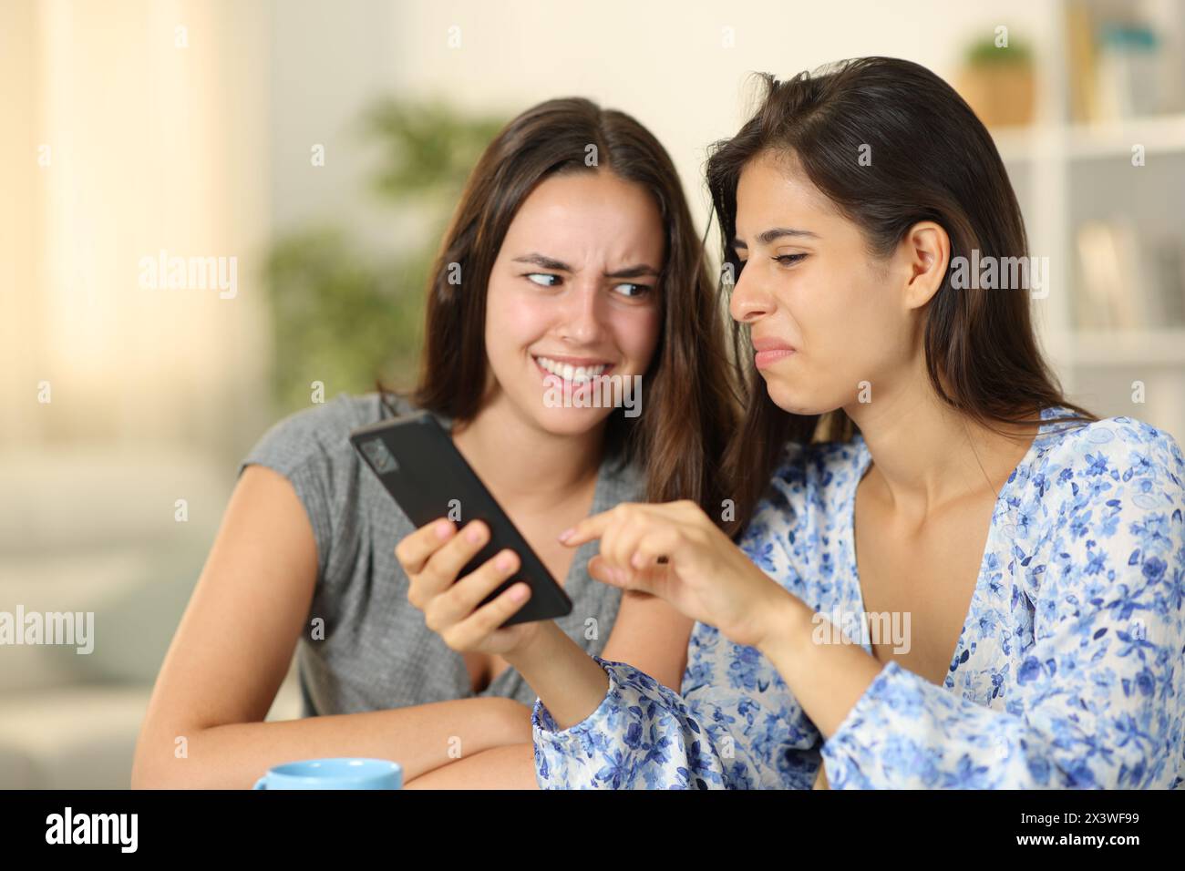 Zwei ekelhafte Frauen, die sich zu Hause böse Inhalte am Telefon anschauen Stockfoto