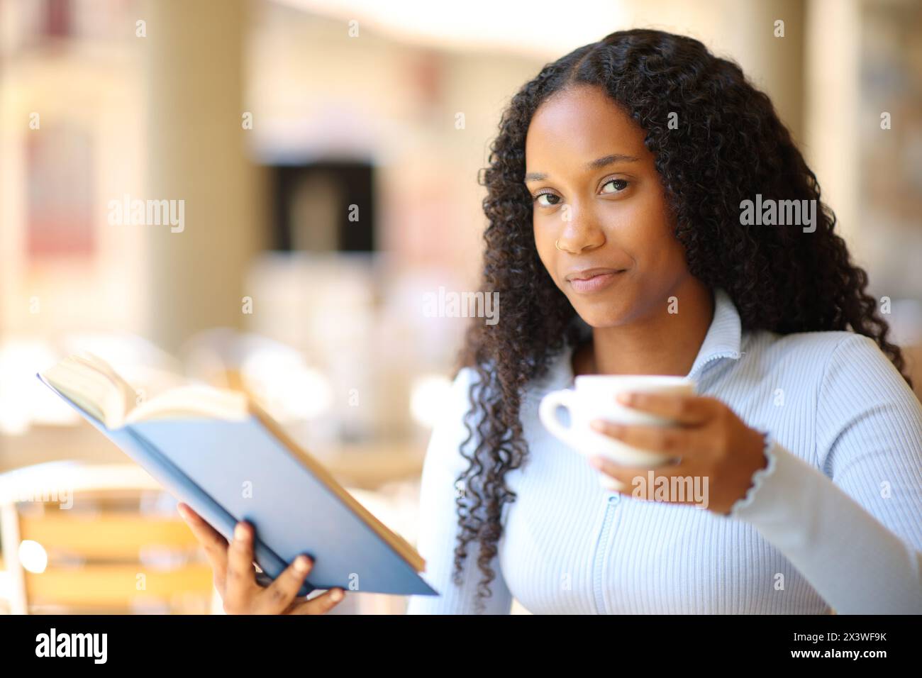 Glückliche schwarze Frau mit Papierbuch und Kaffeetasse, die Sie auf einer Restaurantterrasse ansieht Stockfoto