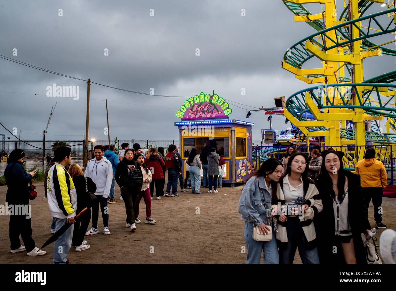 Die Leute stehen an, um eine Achterbahn in einem Vergnügungspark zu fahren, der sich im Parc del Forum von Barcelona befindet, anlässlich der Feier der Aprilmesse (Feria de Abril). Die Feria de Abril in Barcelona ist ein Volksfest andalusischer Wurzeln, das seit fast 50 Jahren in Katalonien gefeiert wird. Stockfoto