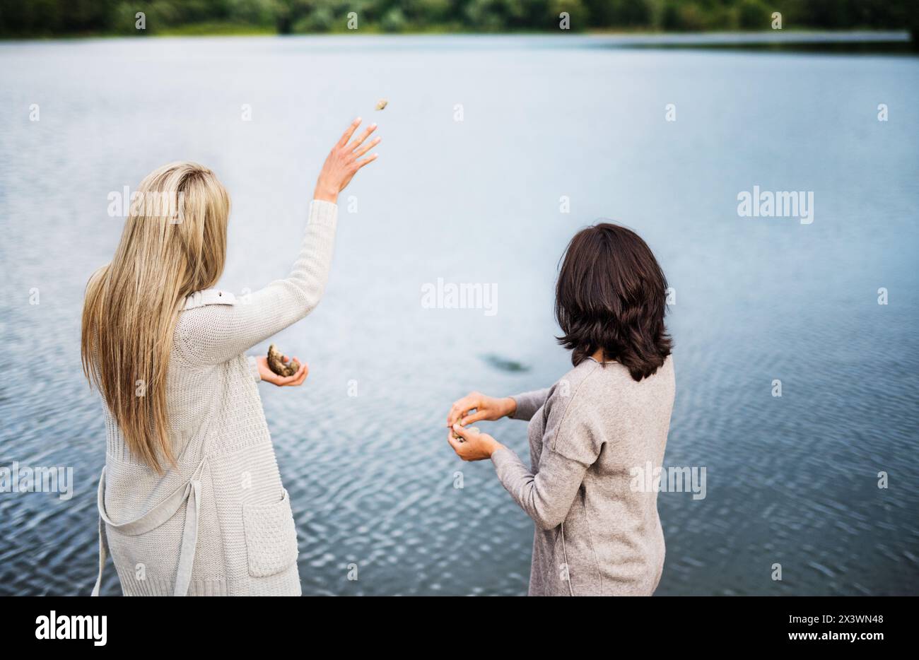 Mutter und Tochter draußen, zu Fuß am Stausee, am Ufer des Sees, werfen Steine ins Wasser. Bedingungslose, tiefe mütterliche Liebe, Muttertag. Stockfoto