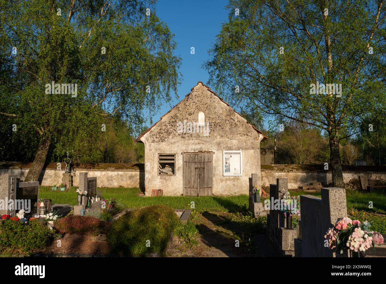 Ungenutzte geschlossene alte Leichenhalle auf einem Landfriedhof in Lodhéřov (Riegerschlag), Tschechien. Gräber stehen vorne. Stockfoto