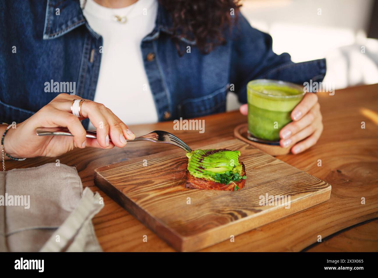 Feminine Hände halten Avocadotoast und grünen Smoothie in einem Restaurant und zeigen vegane gesunde Speisen. Stockfoto