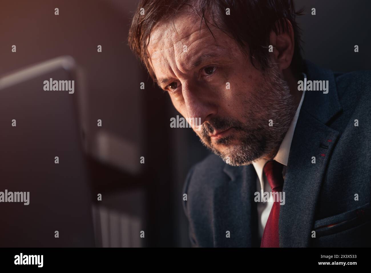 Nahaufnahme Porträt eines müden kaukasischen Geschäftsmannes, der auf den Laptop-Bildschirm schaut, während er spät nachts im Büro arbeitet, selektiver Fokus Stockfoto
