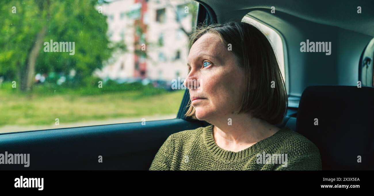 Porträt einer ernsten, reiferen Frau, die auf der Rückbank eines Autos denkt, während sie durch Wohnviertel fährt, selektiver Fokus Stockfoto