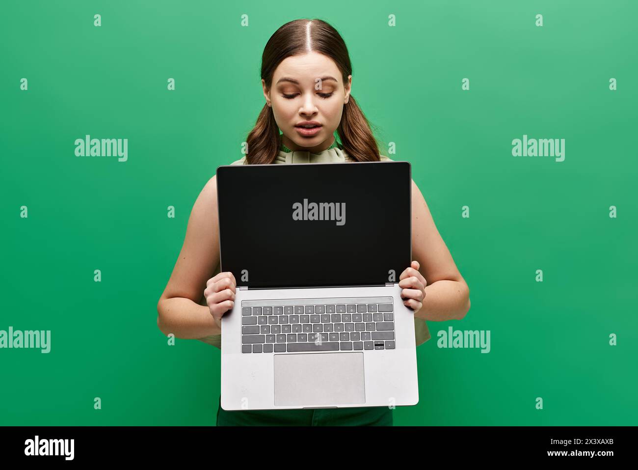 Eine junge Frau im Alter von 20 hält einen Laptop vor ihr Gesicht und verdeckt ihre Identität in einem Studio. Stockfoto