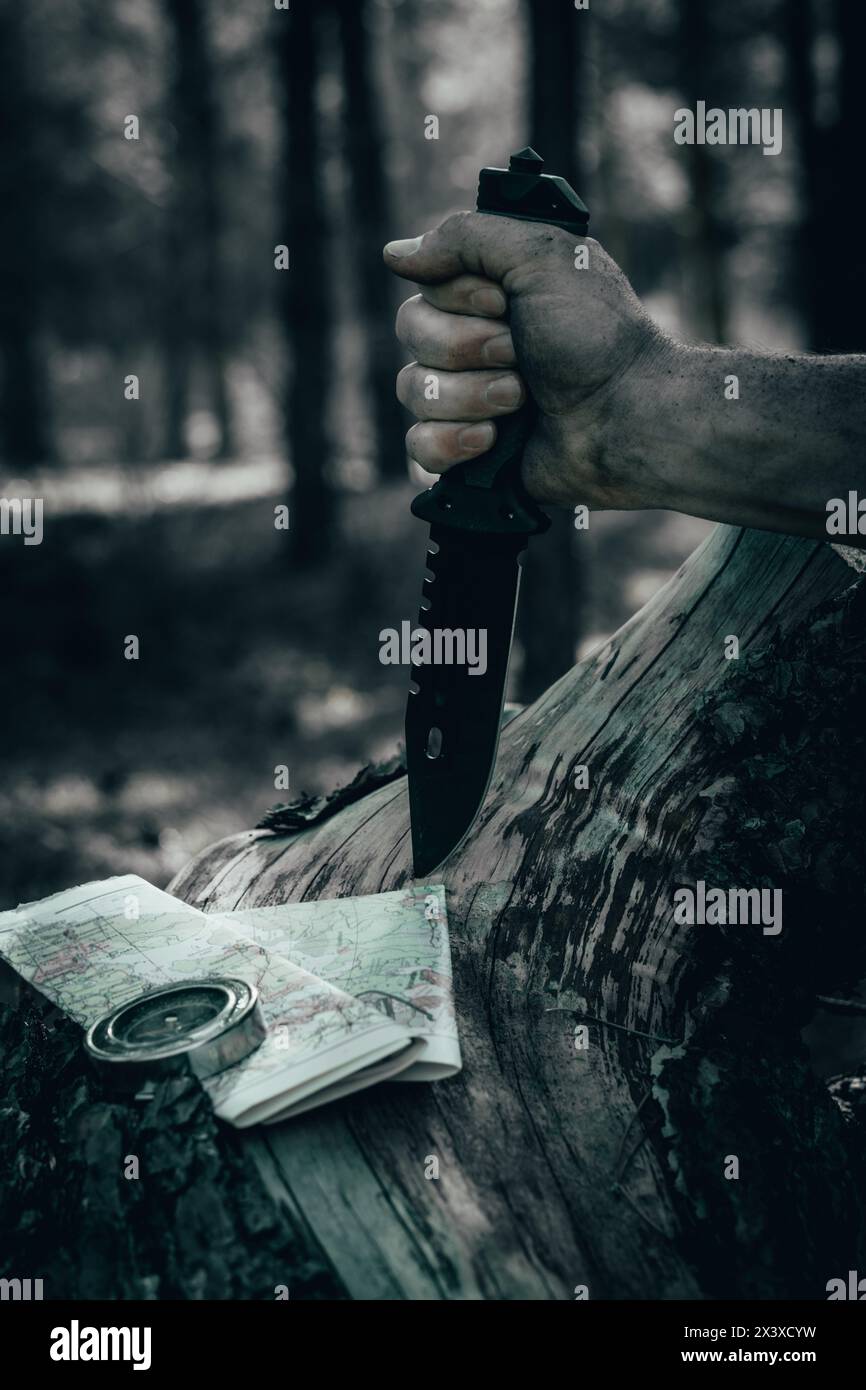 Mann Hand im Wald hält Jagdmesser vor Hintergrund Geländekarte und Kompass. Concept Survival Wildness Stockfoto