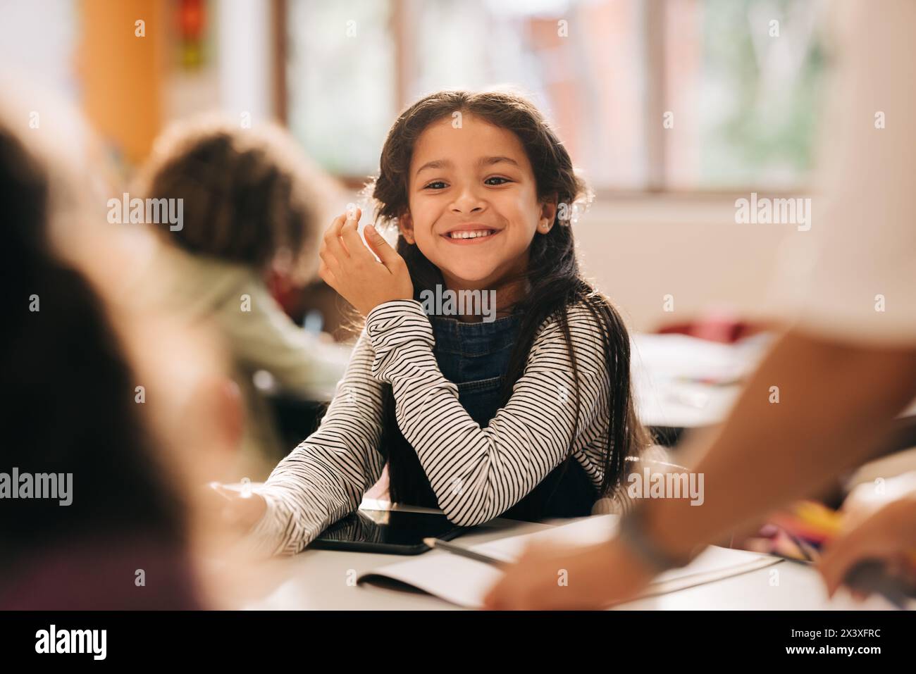 Glückliches kleines Mädchen, das in der Klasse sitzt, junge Schülerin, die die Grundschule genießt. Kind, das in einer Co-Ed-Schule einen Kreativkurs besucht. Stockfoto