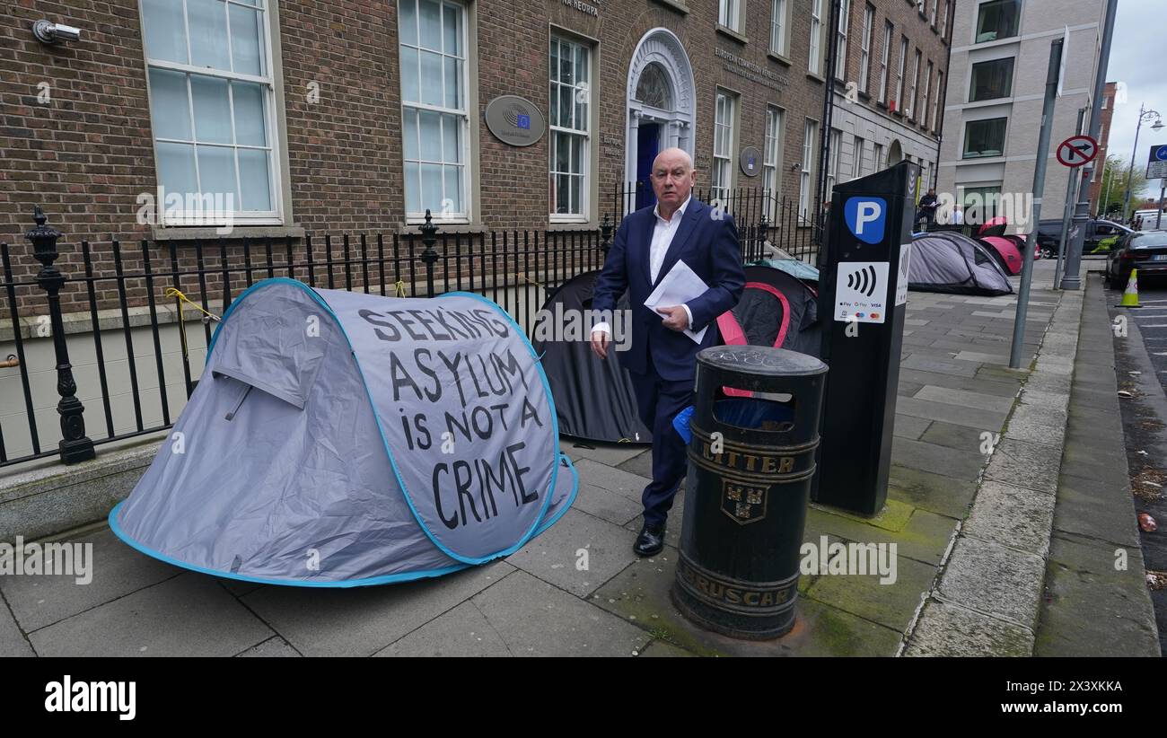 Menschen, die an Zelten vorbeilaufen, in denen Asylbewerber untergebracht sind, in der Nähe des Verbindungsbüros des Europäischen Parlaments in Dublin. Behauptungen, dass die Mehrheit der Asylbewerber aus Nordirland die Grenze überschritten habe, wurden von Menschenrechts- und Flüchtlingsorganisationen in Frage gestellt. Irlands Justizministerin Helen McEntee behauptete letzte Woche, dass die Zahl der Asylbewerber, die von Nordirland in den Staat überquerten, jetzt "über 80 %" sei, nachdem sich die Migrationsmuster in den letzten Monaten verändert hatten. Bilddatum: Montag, 29. April 2024. Stockfoto