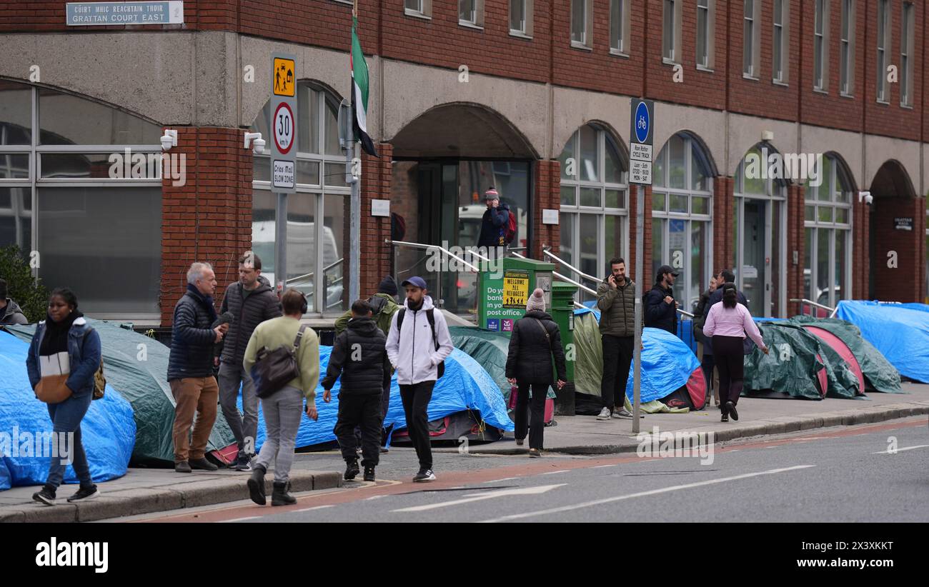 Menschen, die an Zelten vorbeilaufen, in denen Asylbewerber untergebracht sind, in der Nähe des Internationalen Schutzamtes in Dublin. Behauptungen, dass die Mehrheit der Asylbewerber aus Nordirland die Grenze überschritten habe, wurden von Menschenrechts- und Flüchtlingsorganisationen in Frage gestellt. Irlands Justizministerin Helen McEntee behauptete letzte Woche, dass die Zahl der Asylbewerber, die von Nordirland in den Staat überquerten, jetzt "über 80 %" sei, nachdem sich die Migrationsmuster in den letzten Monaten verändert hatten. Bilddatum: Montag, 29. April 2024. Stockfoto