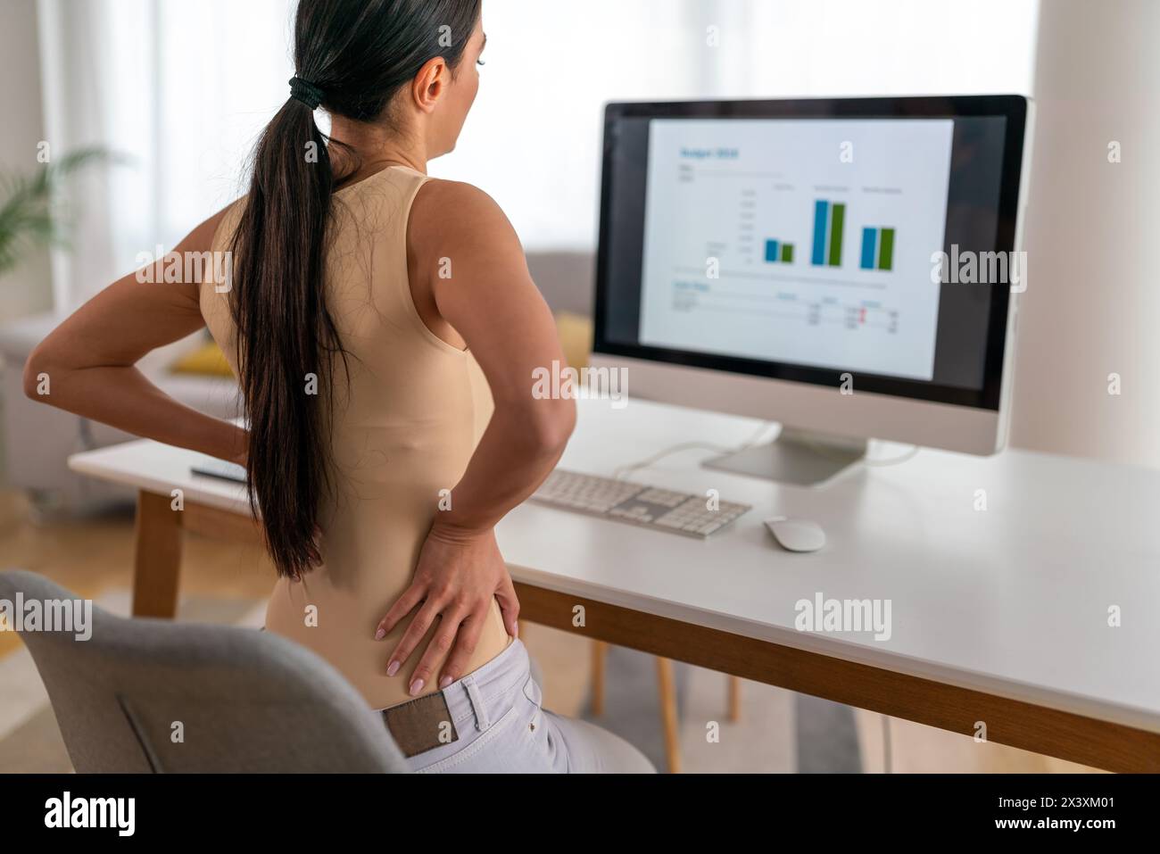 Müde Arbeitnehmerin sitzt am Schreibtisch, Rückenschmerzen leiden, Frau starke Rückenschmerzen, falsche Haltung Stockfoto