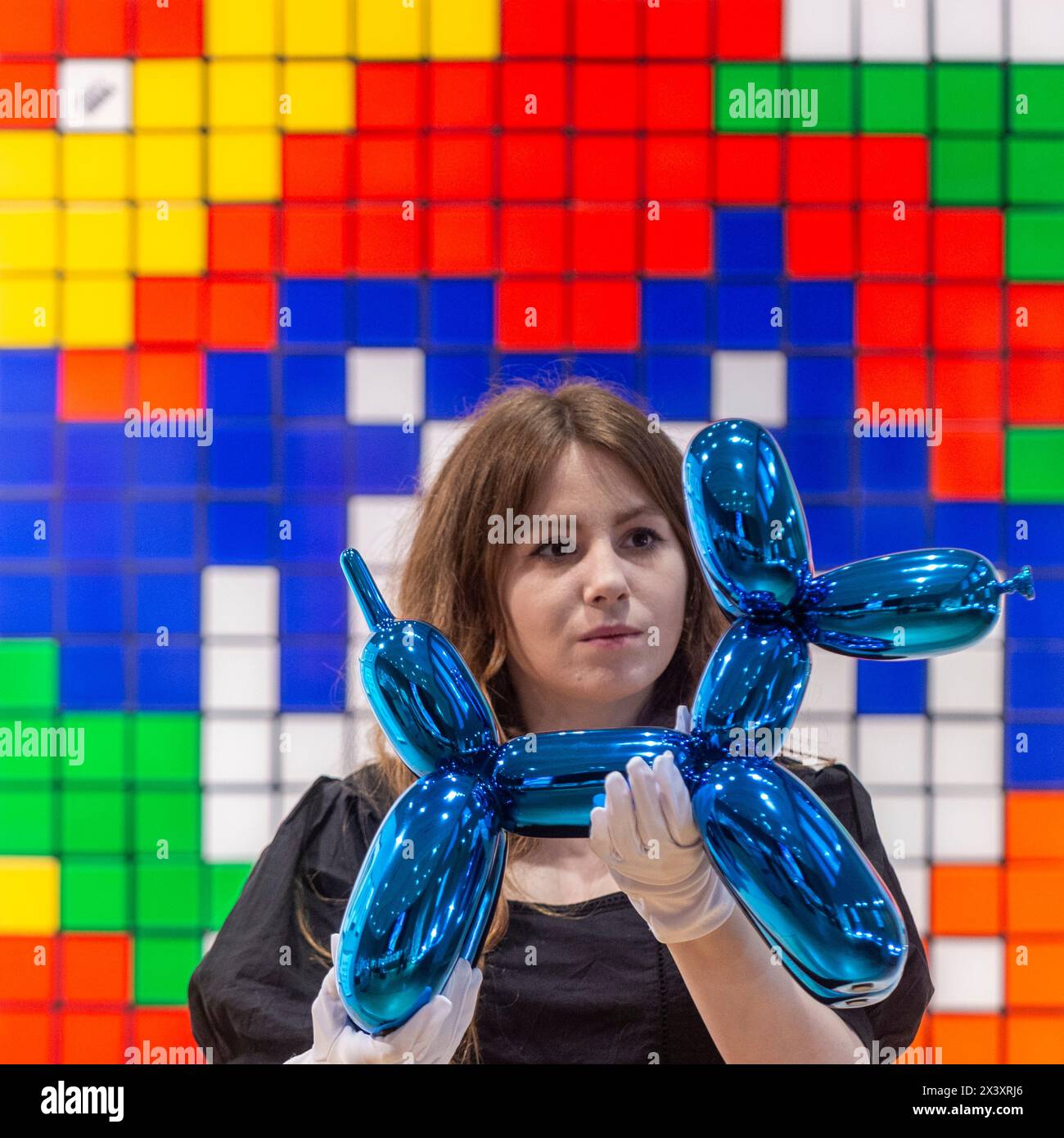 London, Großbritannien. 29. April 2024. Ein Mitarbeiter mit "Balloon Dog (Blue)", 2021, von Jeff Koons, (18.000 £ - 25.000), vor "Rubik Camouflage (NVDR1-2), from Rubikcubism", 2023, (2.000 £ - 3.000 £) von Invader bei der Vorschau von "Hot Off the Press", einem Verkauf von Druckerzeugnissen und Neuauflagen, in den letzten 50 Jahren von bekannten zeitgenössischen Künstlern geschaffen und veröffentlicht. Die Arbeiten werden am 1. Mai in der Bonhams New Bond Street versteigert. Quelle: Stephen Chung / Alamy Live News Stockfoto