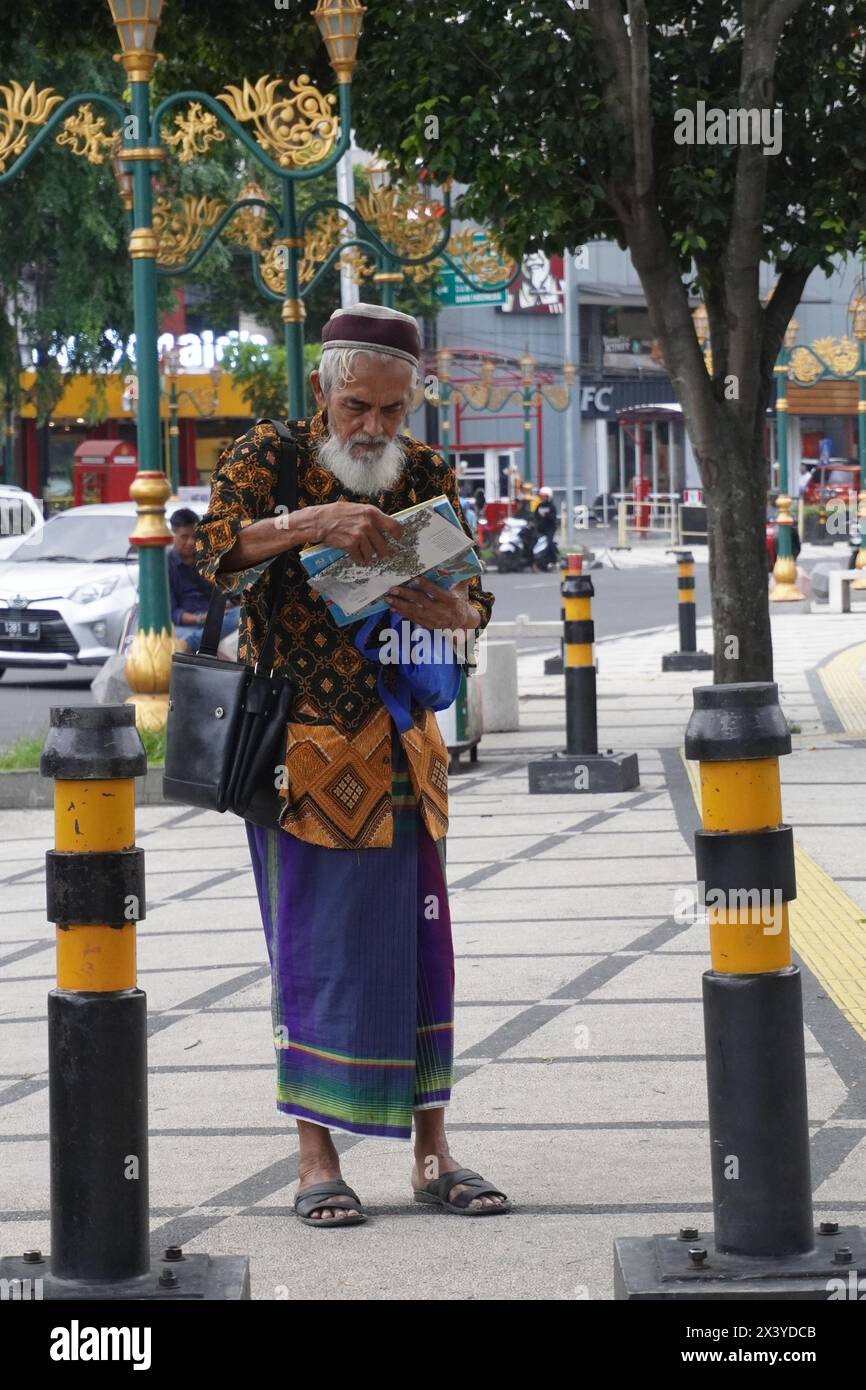 Ein muslimischer Großvater, der auf dem Bürgersteig stand und etwas las Stockfoto