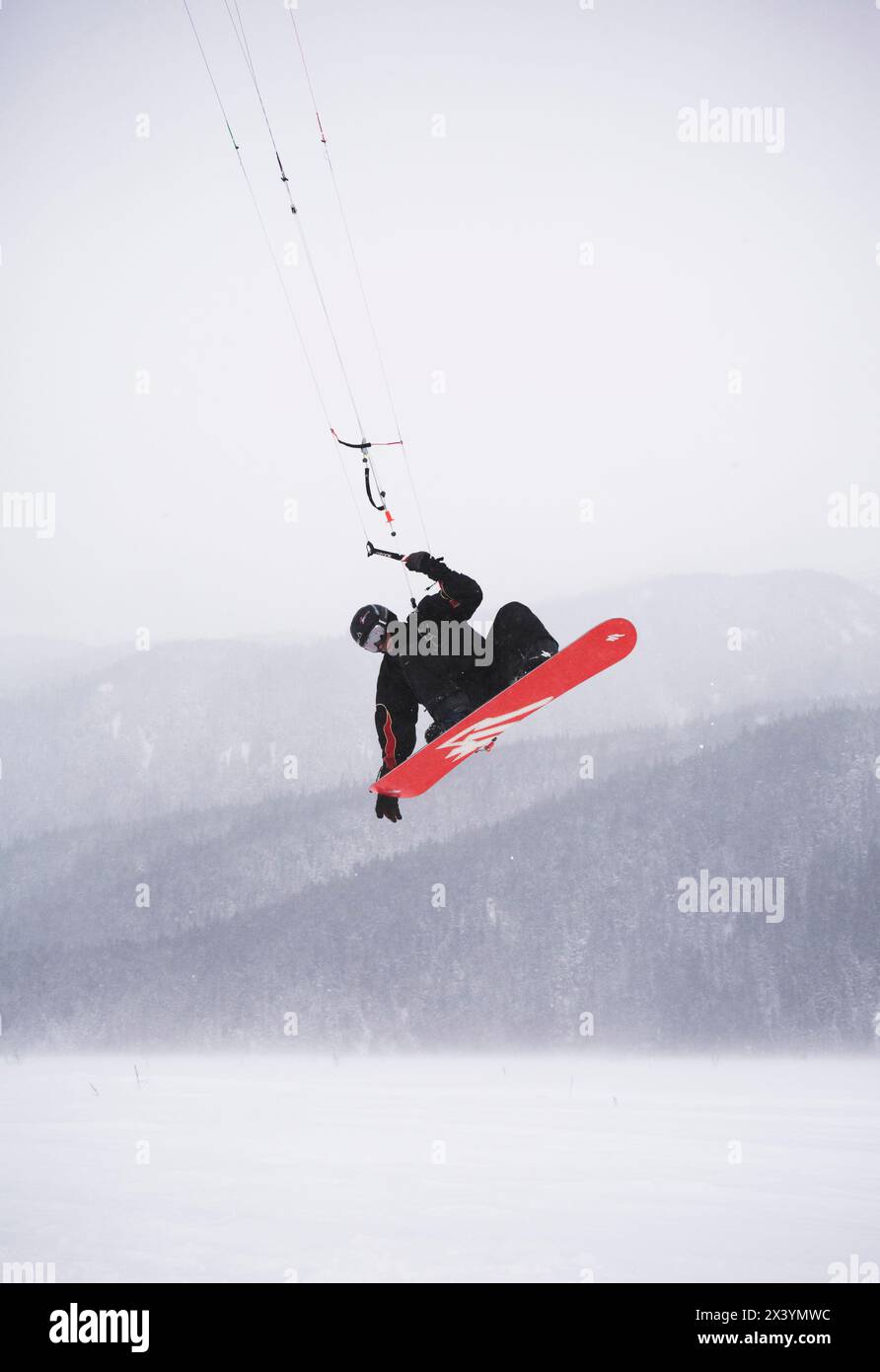 Ein mittelgroßer Mann schnappt sich sein Brett, während er in Alaska im Schnee drackt. Stockfoto