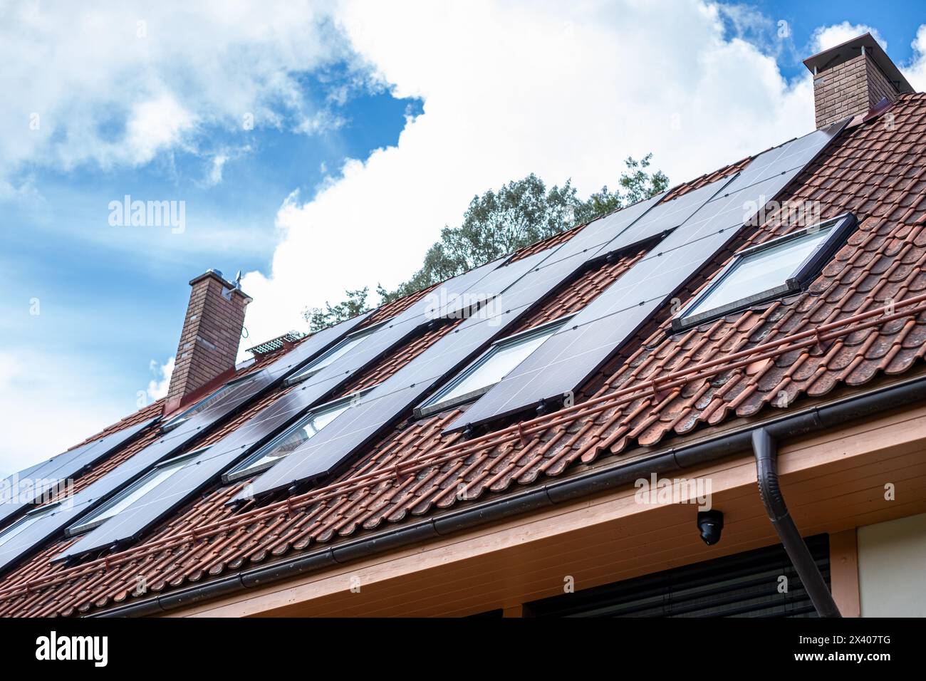 Die Solarinstallation auf dem Dach in einem Familienhaus, vor dem Hintergrund üppiger Bäume und blauer Himmel, zeigt ein Engagement für saubere Energie und Kohlendioxid Stockfoto