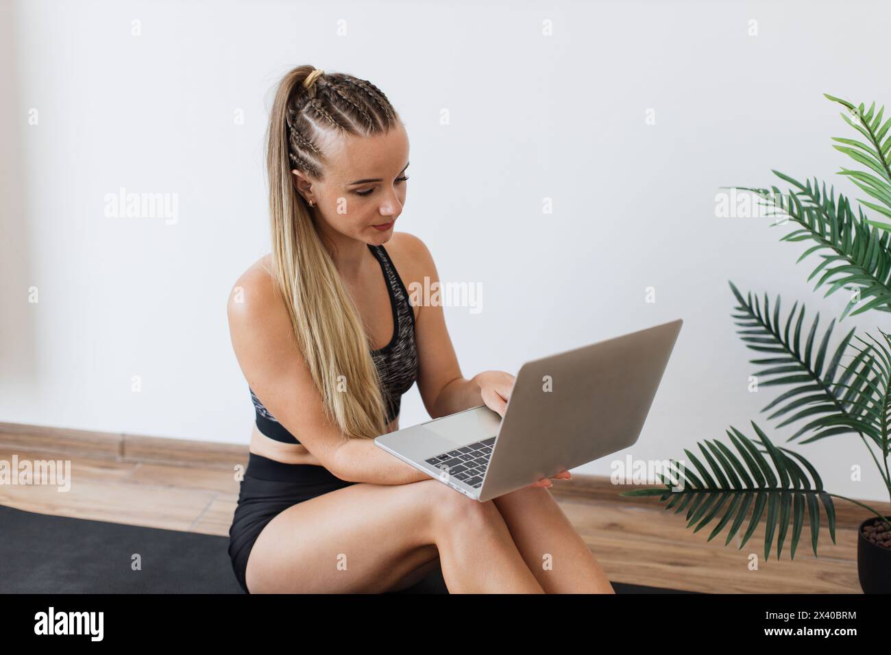 Junge Frau in Fitnesskleidung mit Laptop auf Yogamatte Stockfoto