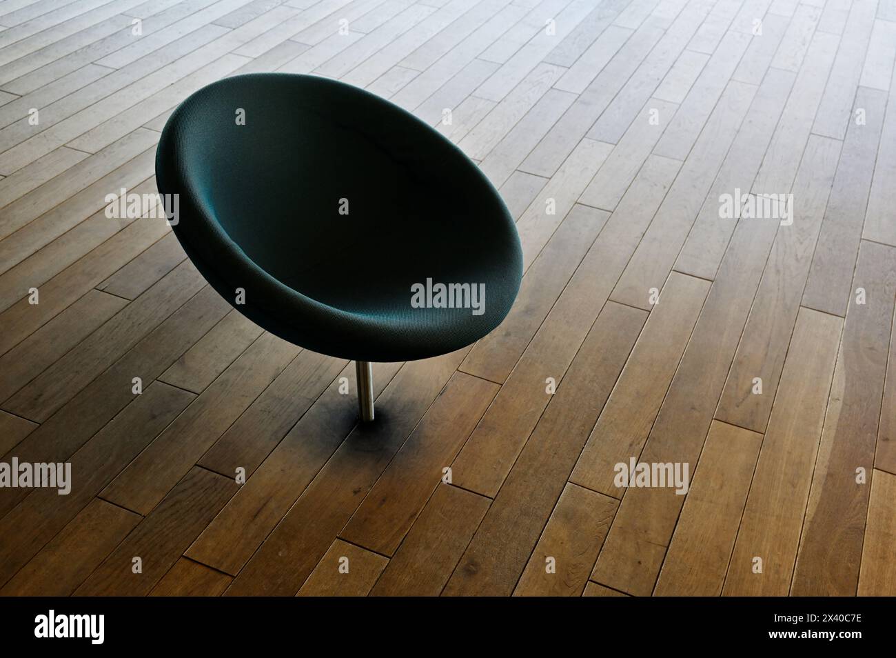 Ein einsamer schwarzer Stuhl steht stoisch auf dem polierten Holzboden, ein markanter Kontrast zu den warmen Tönen des Innenraums Stockfoto