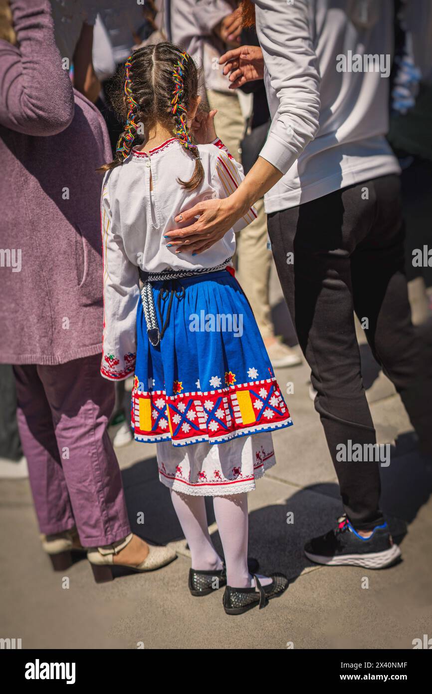 Grundschulmädchen in traditioneller bulgarischer Tracht mit Familie, Volksfest im Freien Rückansicht, nationales Kulturkonzept Stockfoto